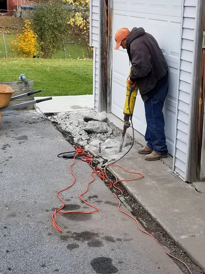 Worker using jackhammer on driveway drainage system